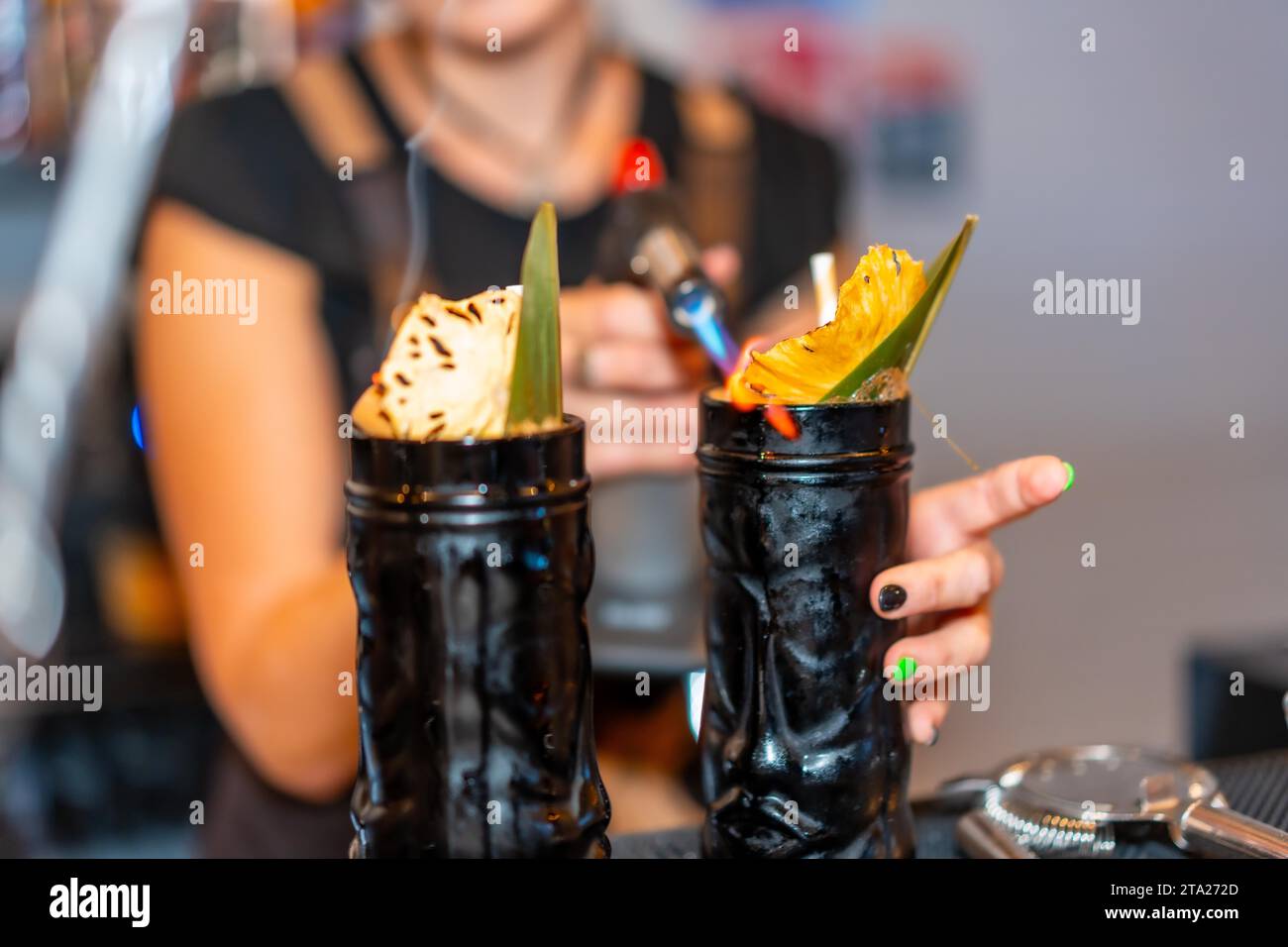 Barista che utilizza una torcia elettrica per infuocare la guarnizione di un cocktail nel bancone di un bar Foto Stock