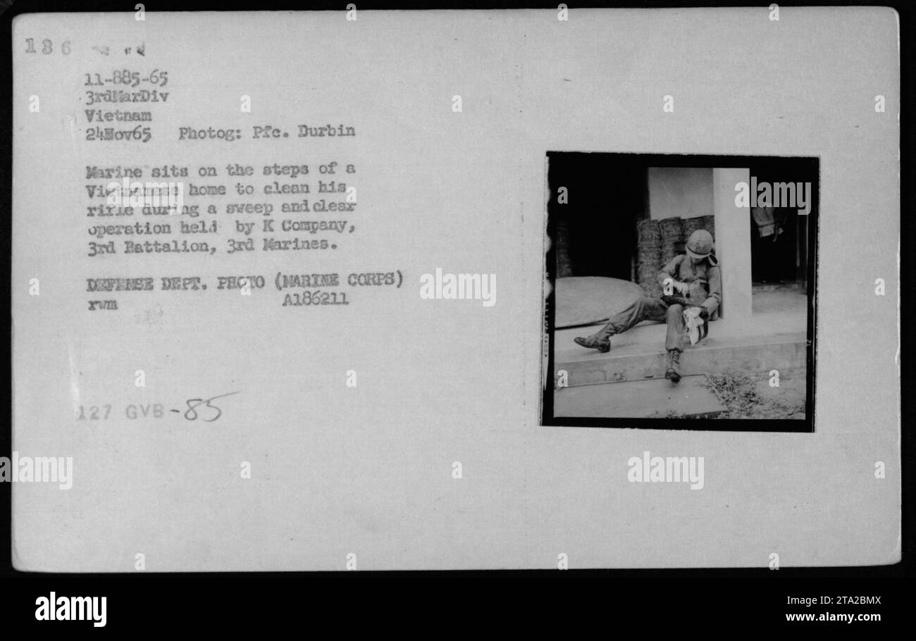 Un soldato marino che pulisce il suo fucile sui gradini di una casa vietnamita durante un'operazione di pulizia in Vietnam. La foto è stata scattata il 24 novembre 1965 da PFE. Durbin, e mostra un membro della K Company, 3rd Battalion, 3rd Marines in azione. Foto Stock