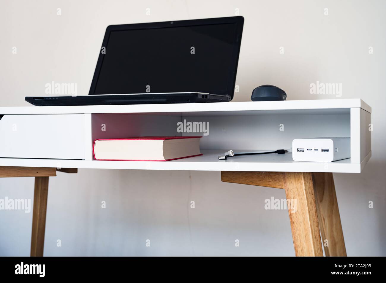 Computer portatile vuoto aperto con mockup e schermo nero su tavolo da scrivania bianco. Libro, mouse e caricabatterie. Area di lavoro minimalista Foto Stock