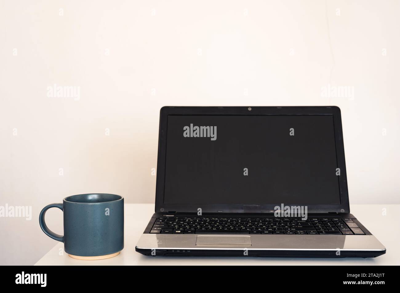 Computer portatile vuoto aperto con mockup e schermo nero su tavolo da scrivania bianco. Tazza con caffè. Area di lavoro minimalista Foto Stock