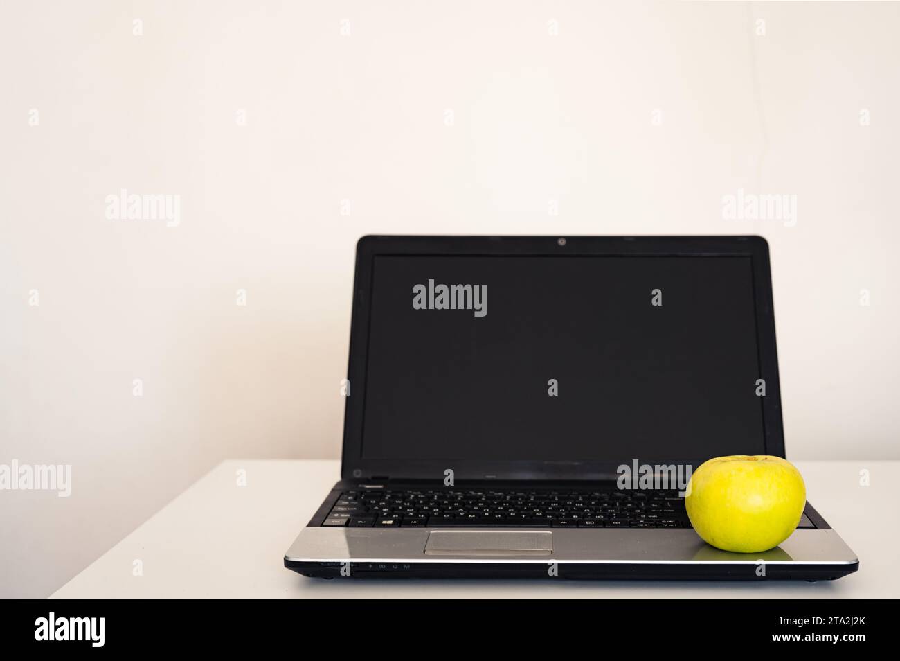 Computer portatile vuoto aperto con mockup e schermo nero su tavolo da scrivania bianco. Mela gialla. Area di lavoro minimalista Foto Stock
