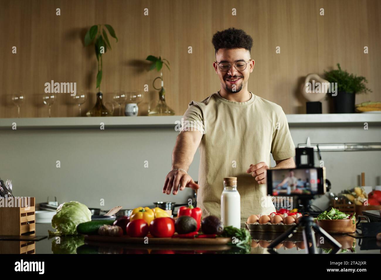 Ripresa media di un giovane cuoco medio orientale che punta il cibo sul tavolo della cucina mentre viene filmato con una fotocamera per smartphone Foto Stock