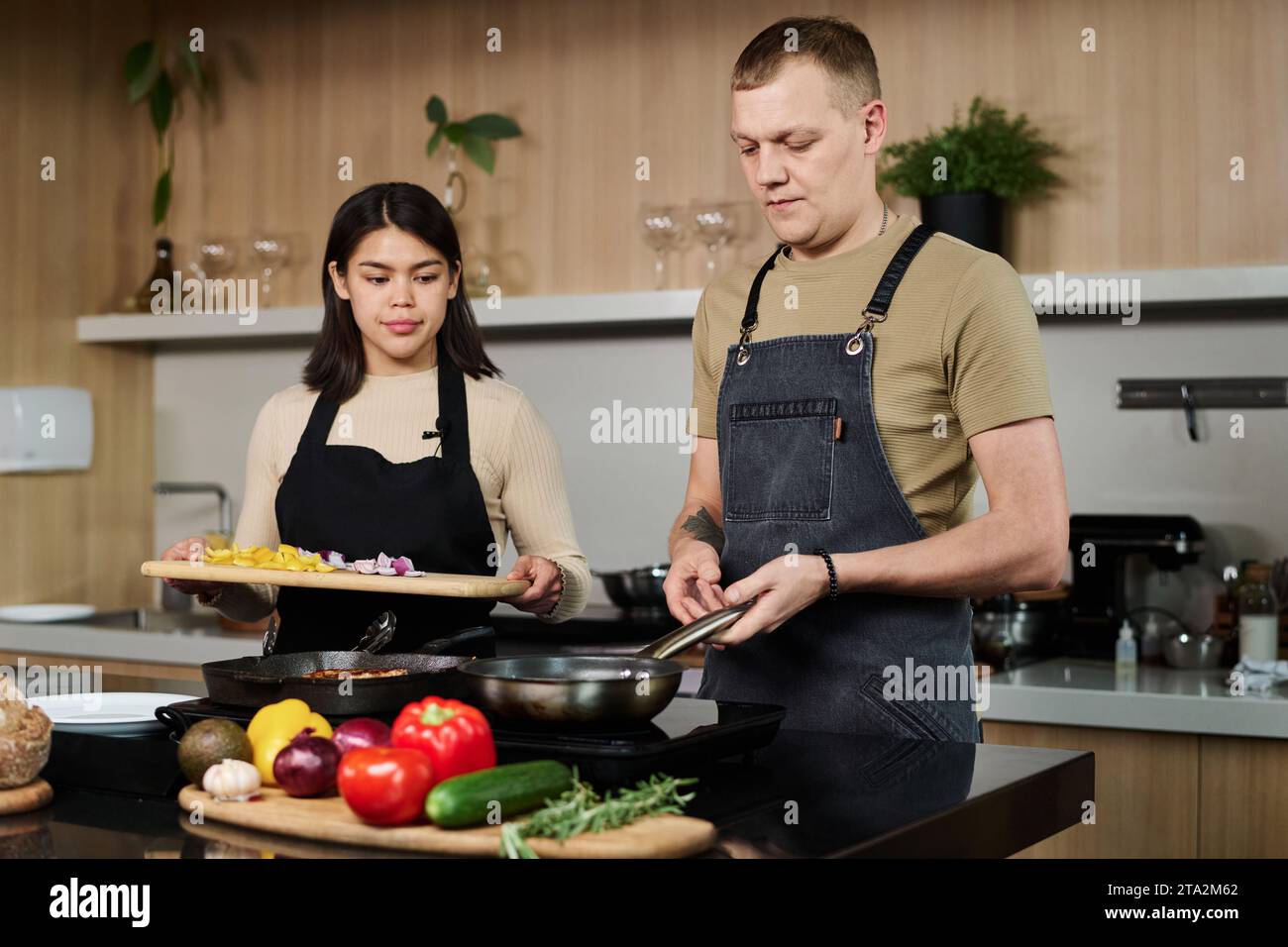Shot medio di una giovane donna ispanica e di uno chef caucasico in cucina per friggere le verdure tritate in padella Foto Stock