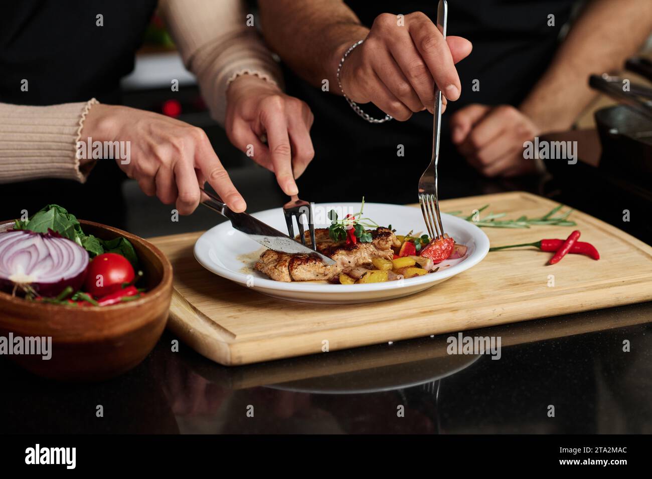 Primo piano delle mani di un uomo e una donna irriconoscibili che mangiano bistecche e verdure da un unico piatto tagliando il cibo a pezzi Foto Stock