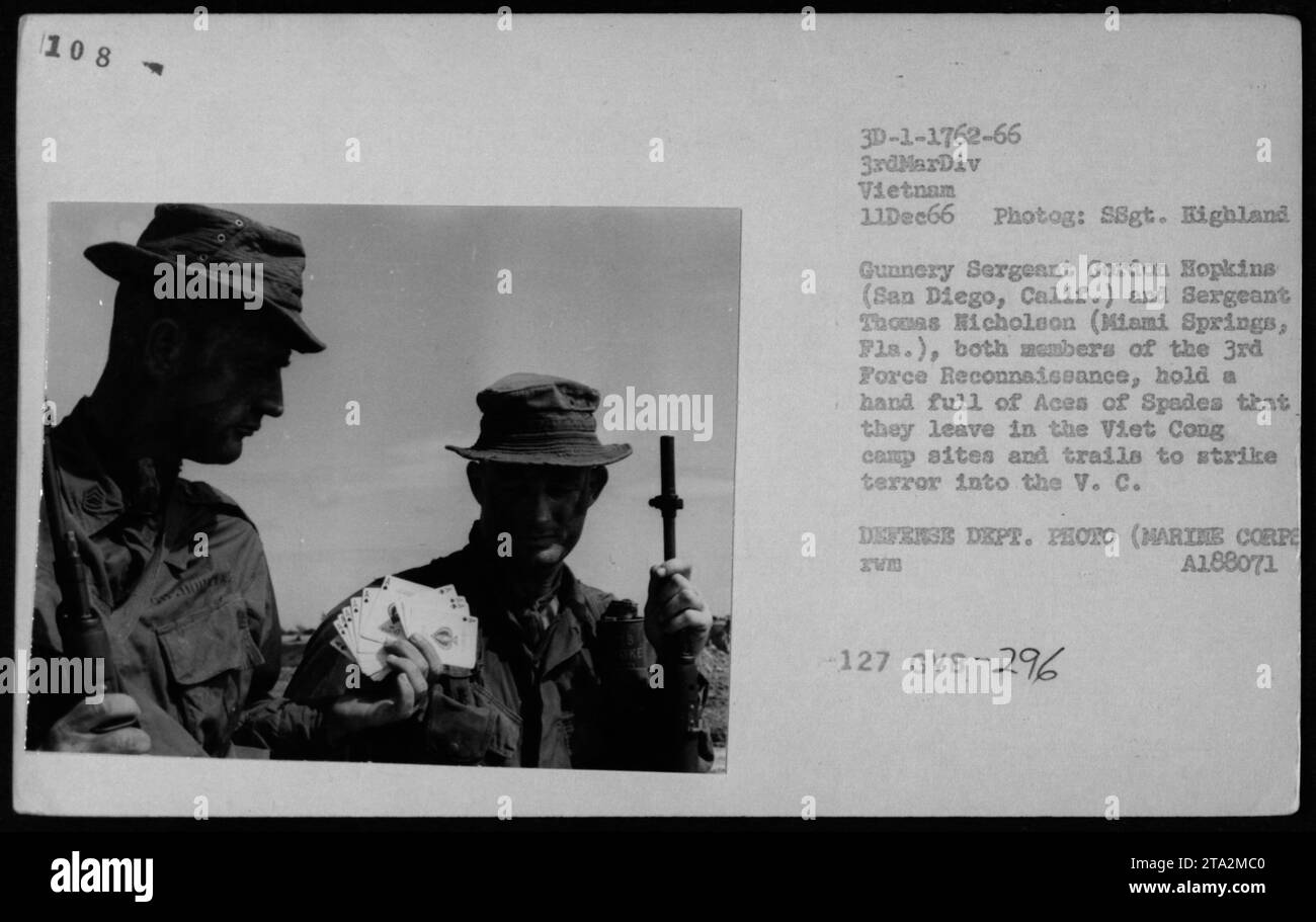 Il sergente Gunnery Gordon Hopkins e il sergente Thomas Nicholson, membri della 3rd Force Reconnaissance in Vietnam, tengono e lasciano una manciata di Aces of Spades nei campi Viet Cong e sentieri per instillare paura. Questa tattica fu impiegata dai Marines per scongiurare la VC durante la guerra. Foto scattata l'11 dicembre 1966. Foto Stock