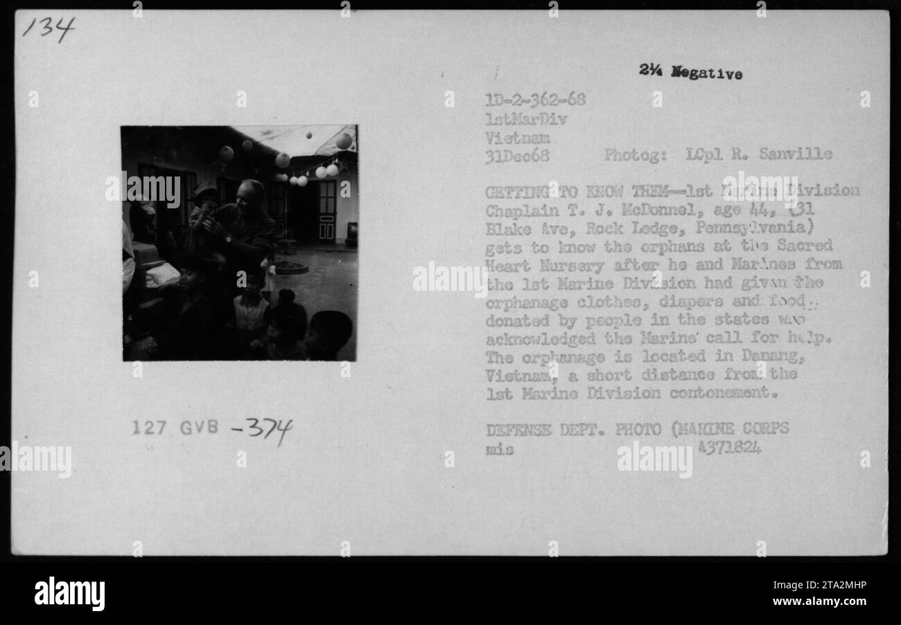 Il cappellano T. J. McDonnel interagisce con gli orfani della Sacred Heart Nursery di Danang, in Vietnam, mentre riceve vestiti, pannolini e donazioni di cibo dagli Stati Uniti vicino alla base della 1st Marine Division nel 1968. Foto Stock