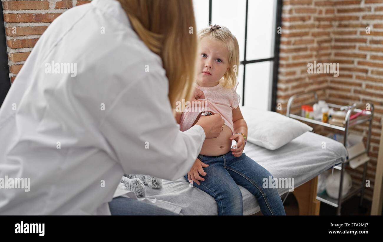Pediatra premuroso in clinica esaminando il torace del paziente bambino adorabile utilizzando lo stetoscopio, garantendo respiro abbondante durante l'esame medico in accogliente guarigione interna Foto Stock