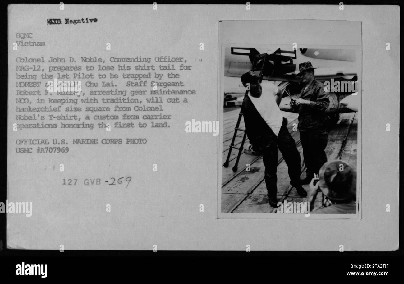 Il colonnello John D. Noble, ufficiale comandante del MAG-12, si prepara a tagliare la coda della camicia come risultato di essere stato il primo pilota ad essere intrappolato dal MOREST a MCALF a Chu Lai, in Vietnam. Il sergente maggiore Robert F. Murray, la manutenzione degli attrezzi d'arresto NOO, segue la tradizione di tagliare un quadrato delle dimensioni di un fazzoletto dalla camicia del colonnello Noble. Questa usanza, derivata dalle operazioni della portaerei, onora il primo pilota ad atterrare. Foto Stock