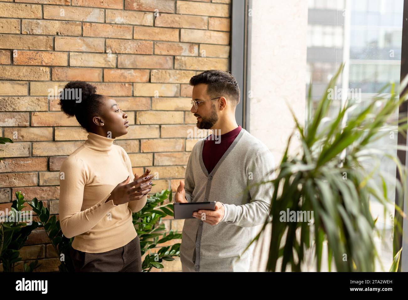 Bella giovane coppia di aziende multietniche con tablet digitali in piedi e discutere in un ufficio moderno Foto Stock