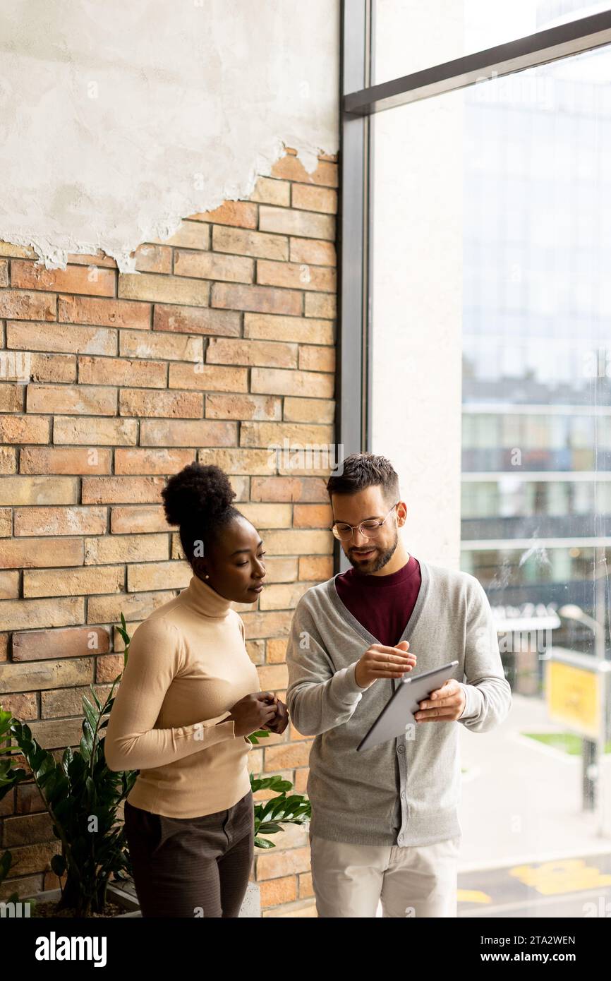 Bella giovane coppia di aziende multietniche con tablet digitali in piedi e discutere in un ufficio moderno Foto Stock