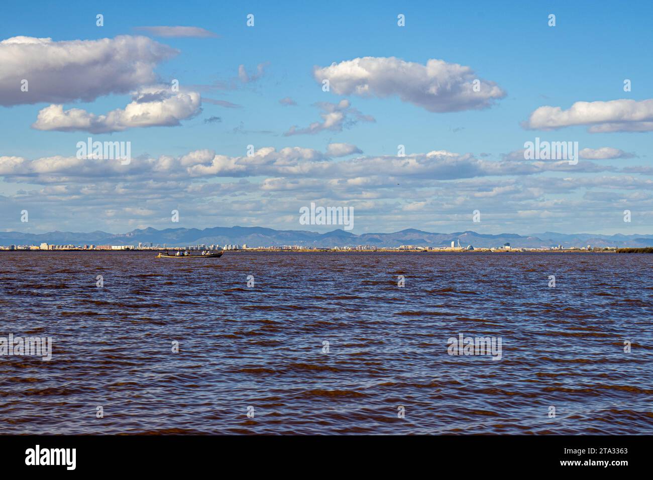 Vista in barca del lago Albufera e c'è una barca con persone su di essa e all'orizzonte in lontananza si può vedere Valencia, Spagna Foto Stock