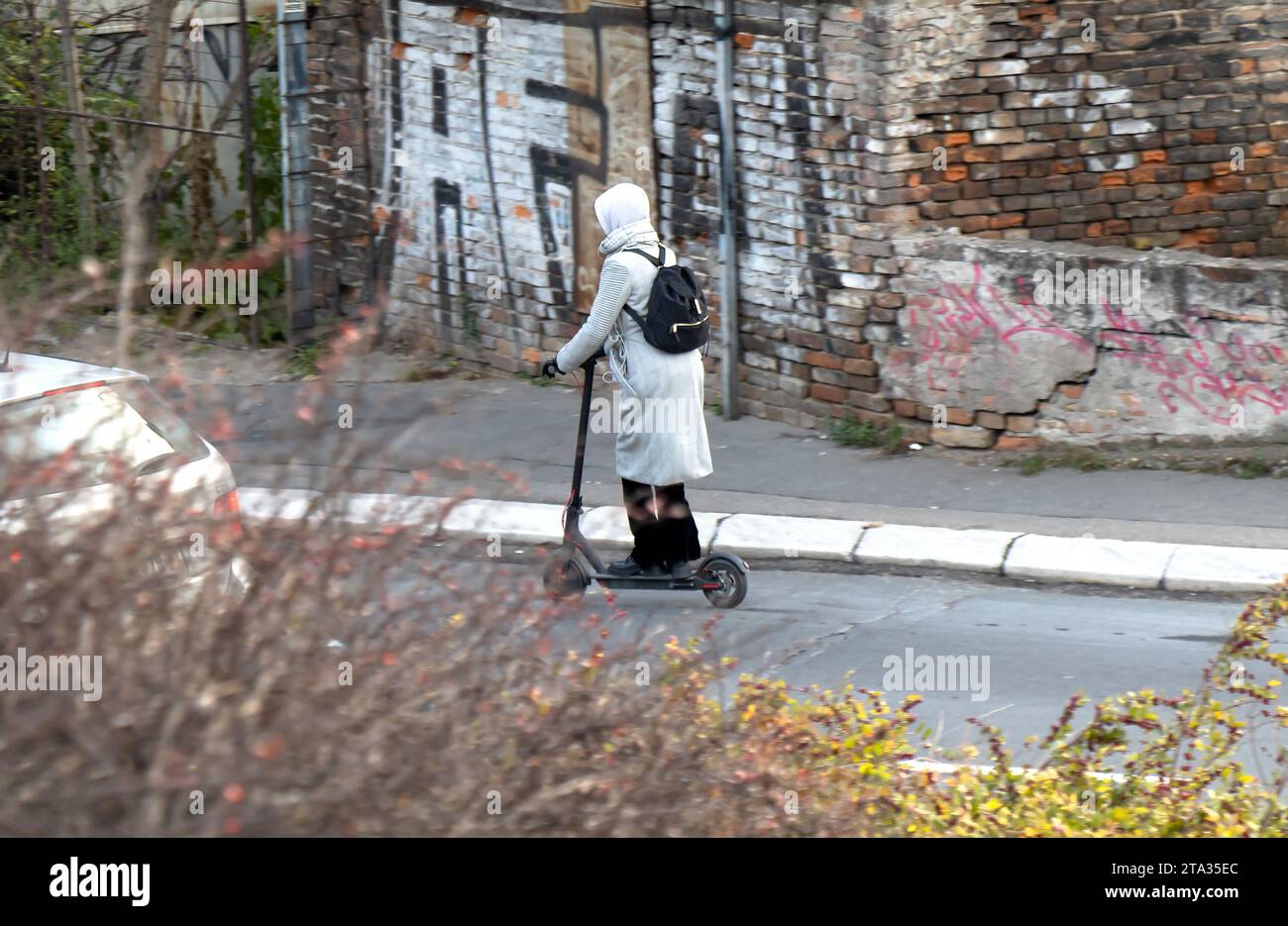 Belgrado, Serbia - 02 dicembre 2020: Una donna che guida uno scooter elettrico in una strada urbana, in inverno, da dietro Foto Stock