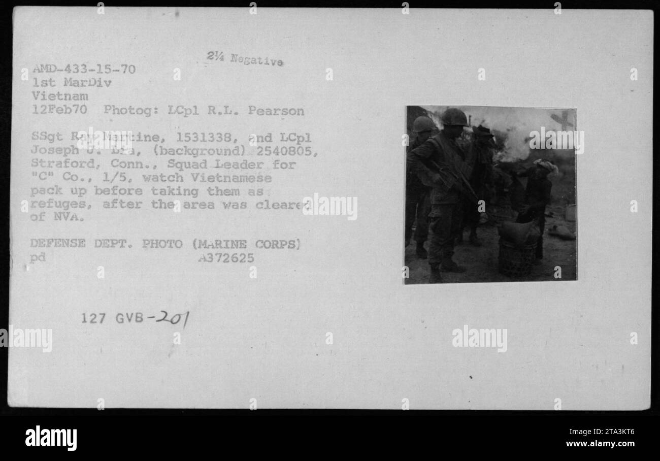 Il personale militare americano guarda come i civili vietnamiti impacchettano i loro averi prima di essere presi come rifugiati, dopo la bonifica di un'area un tempo occupata dalle forze NVA. Questa foto è stata scattata il 12 febbraio 1970 da LCpl R.L. Pearson e mostra SSgt Ray Martine e LCpl Joseph J. Lia sullo sfondo, con LCpl Lia che funge da leader della squadra per 'c' Co., 1/5. Questa immagine fa parte della collezione che illustra le attività militari americane durante la guerra del Vietnam. Foto Stock