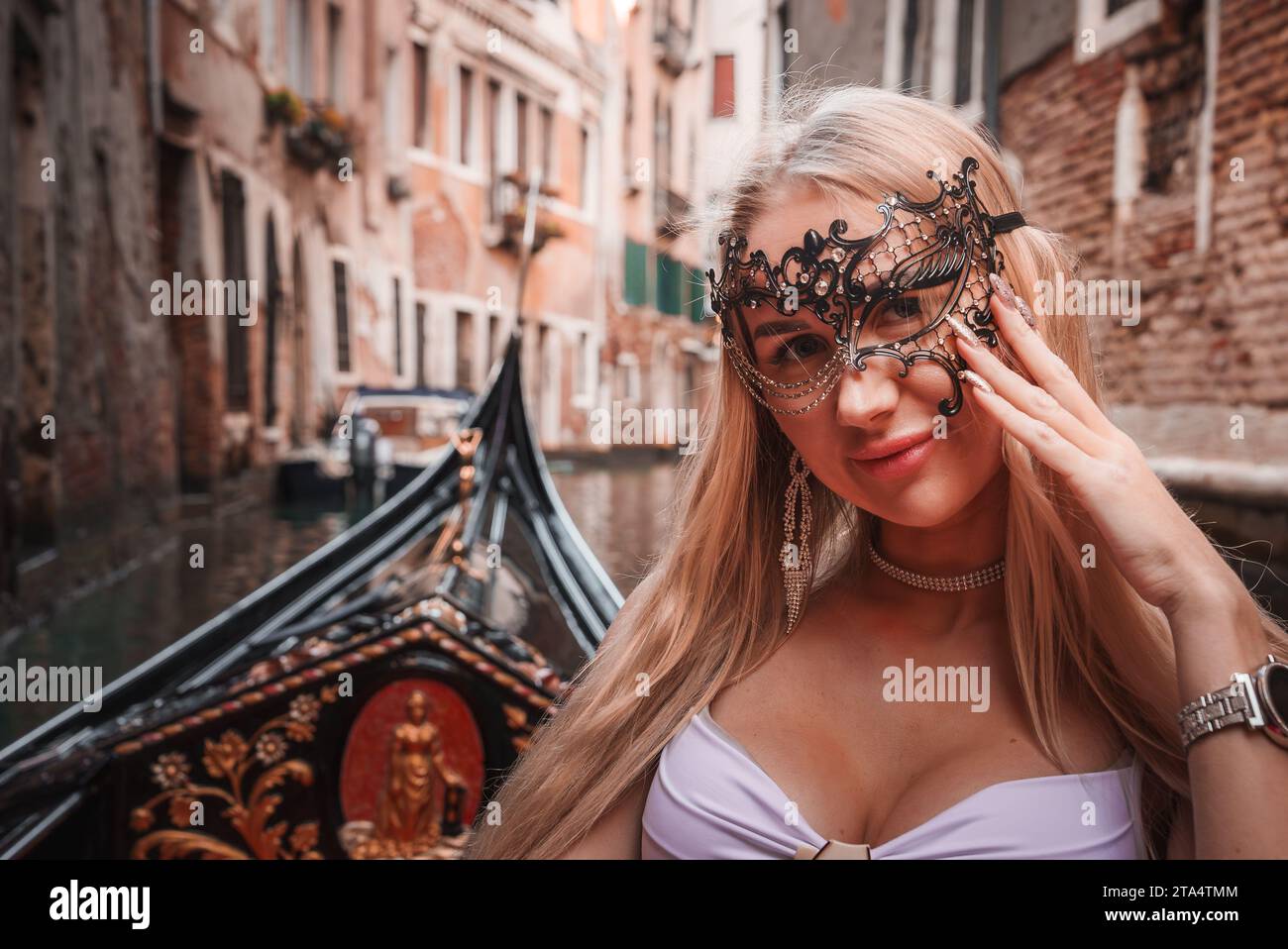 Elegante donna in maschera veneziana seduta sulla gondola nella pittoresca Venezia, Italia. Foto Stock