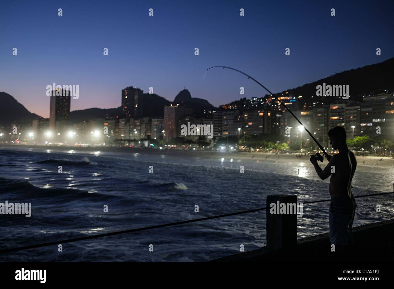 Gente che pesca a Mureta do Leme, Rio de Janeiro, Brasile. Spiaggia di Leme al tramonto, Cristo Redentore e favela Morro da Babilonia al centro dietro gli edifici sul lungomare. Foto Stock