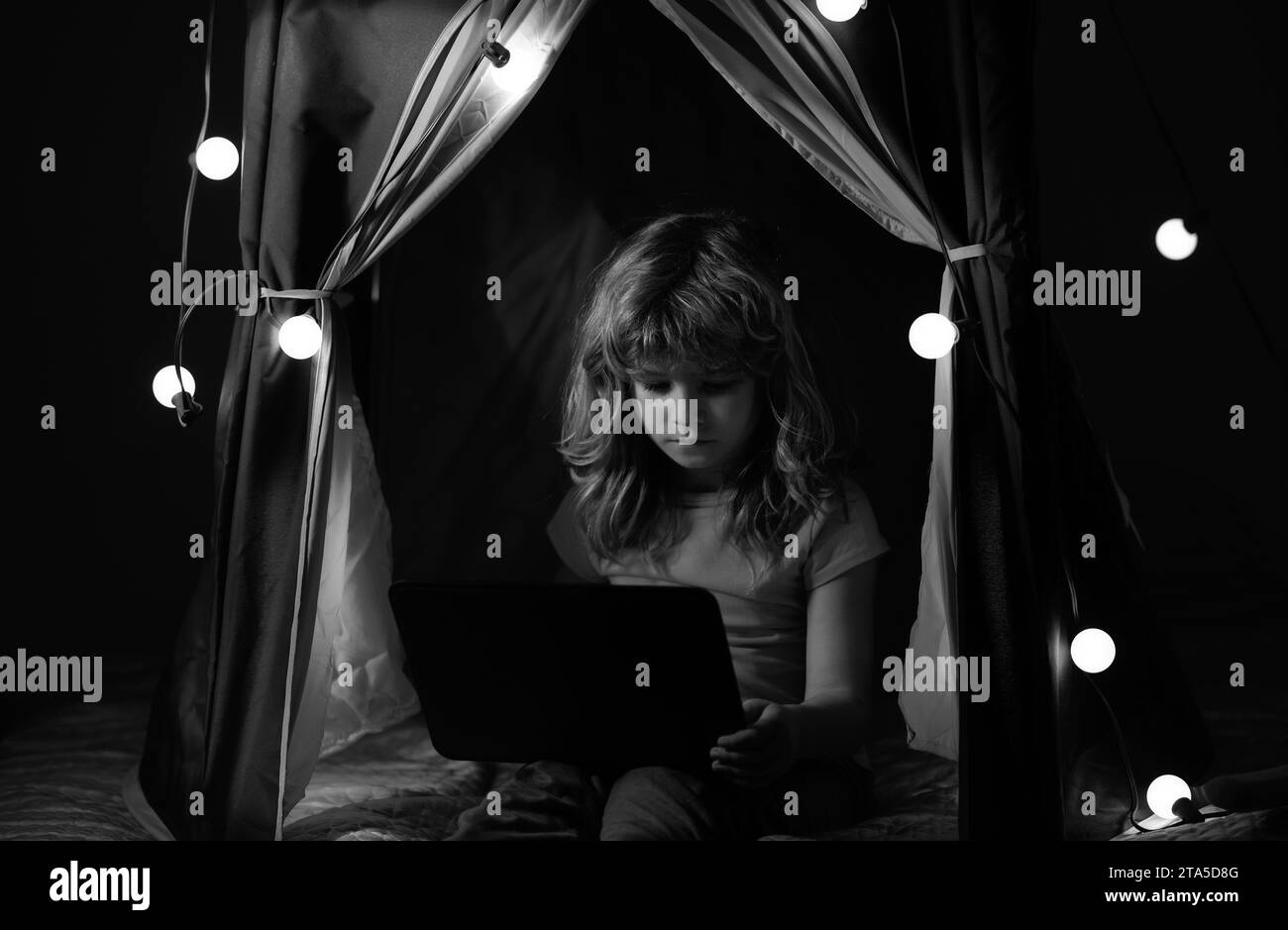 Bambino seduto in tenda di casa giocando con il laptop. Social media per bambini. Foto Stock