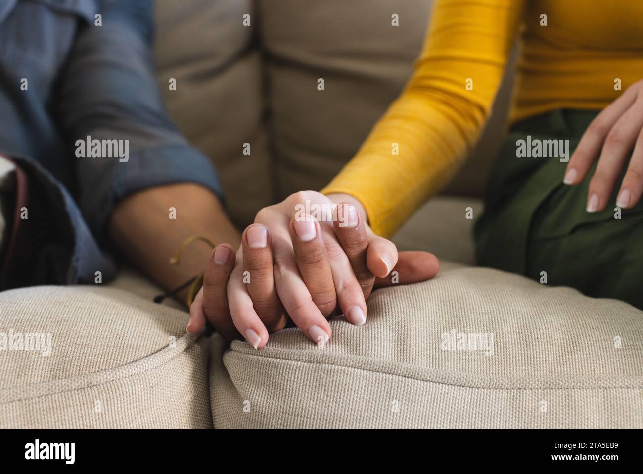 Coppie diverse sedute sul divano e che si tengono per mano nel salotto di casa, spazio per la copia. Gesticolazione, amore, insieme e vita domestica inalterati. Foto Stock