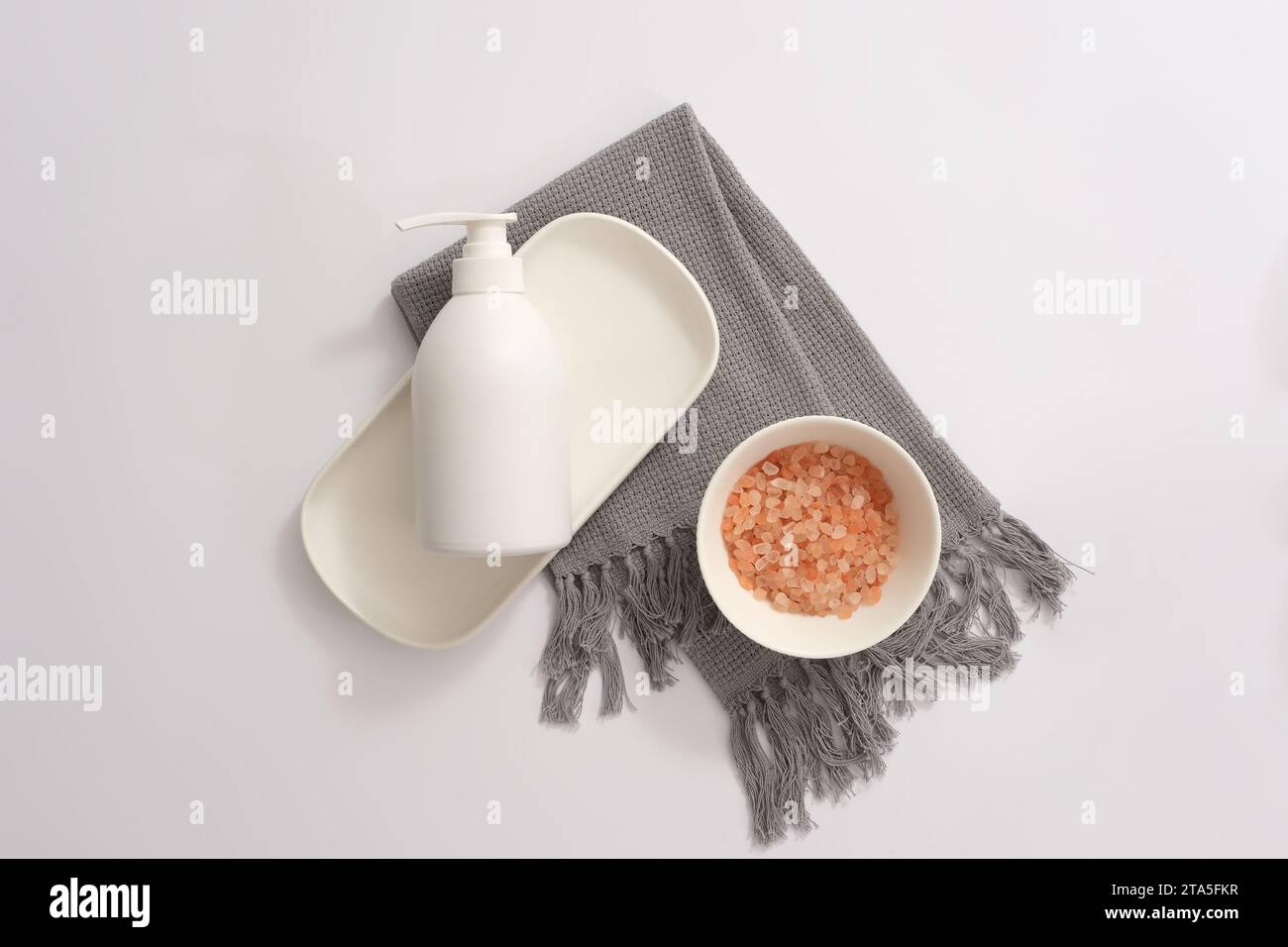 Ciotola in ceramica contenente sale rosa himalayano e bottiglia di pompaggio con etichetta vuota decorata su una sciarpa grigia. Alcuni sostengono che il sale himalayano sia più naturale di Foto Stock