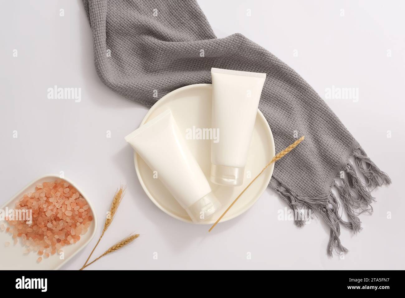 Piatto di forma rotonda con due provette bianche senza etichetta. Un piatto di sale rosa dell'himalaya esposto con una sciarpa. Concetto di routine quotidiana per la cura di sé Foto Stock