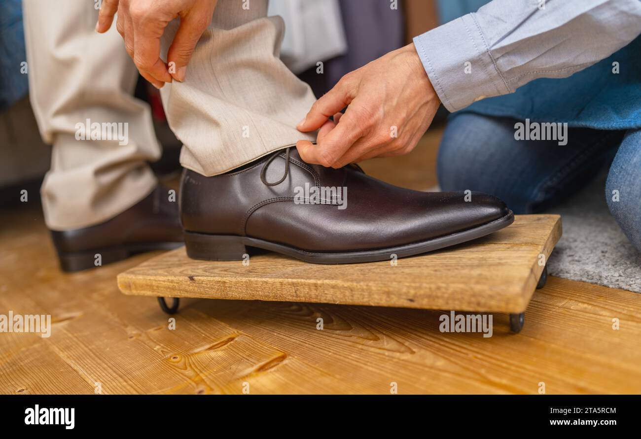 Tailor regola la lunghezza del pantalone da uomo su una scarpa marrone su un poggiapiedi in legno Foto Stock