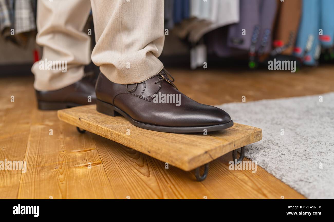 Uomo che prova scarpe di pelle marrone, in piedi su un piede su una tavola di legno Foto Stock