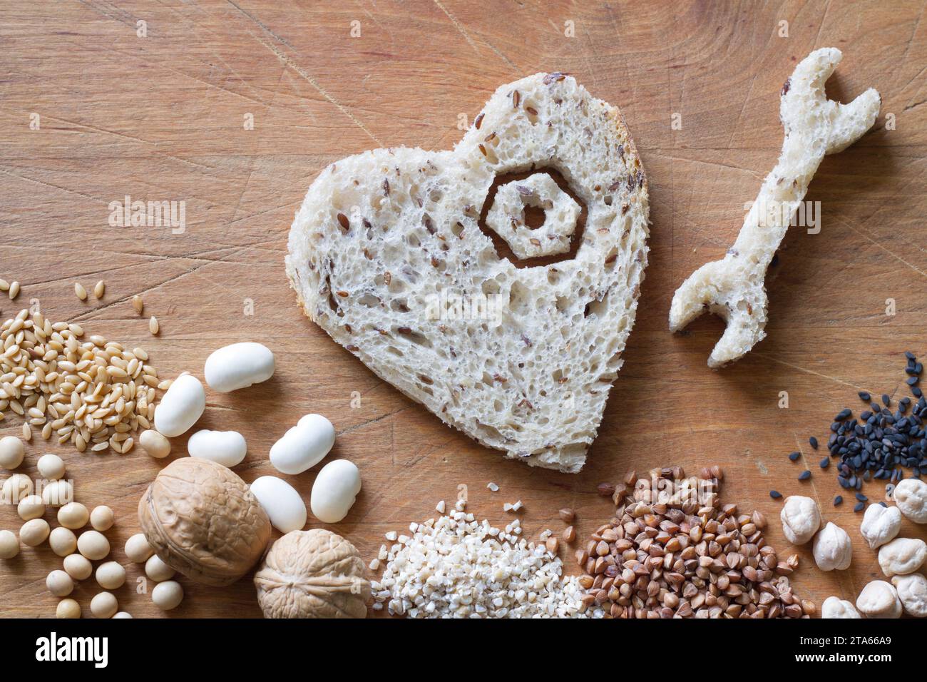 Prodotti a grani interi, semole, noci, legumi, semi su fondo di legno. Chiave, vite e cuore fatto di pane, sano concetto di dieta cuore astratto Foto Stock