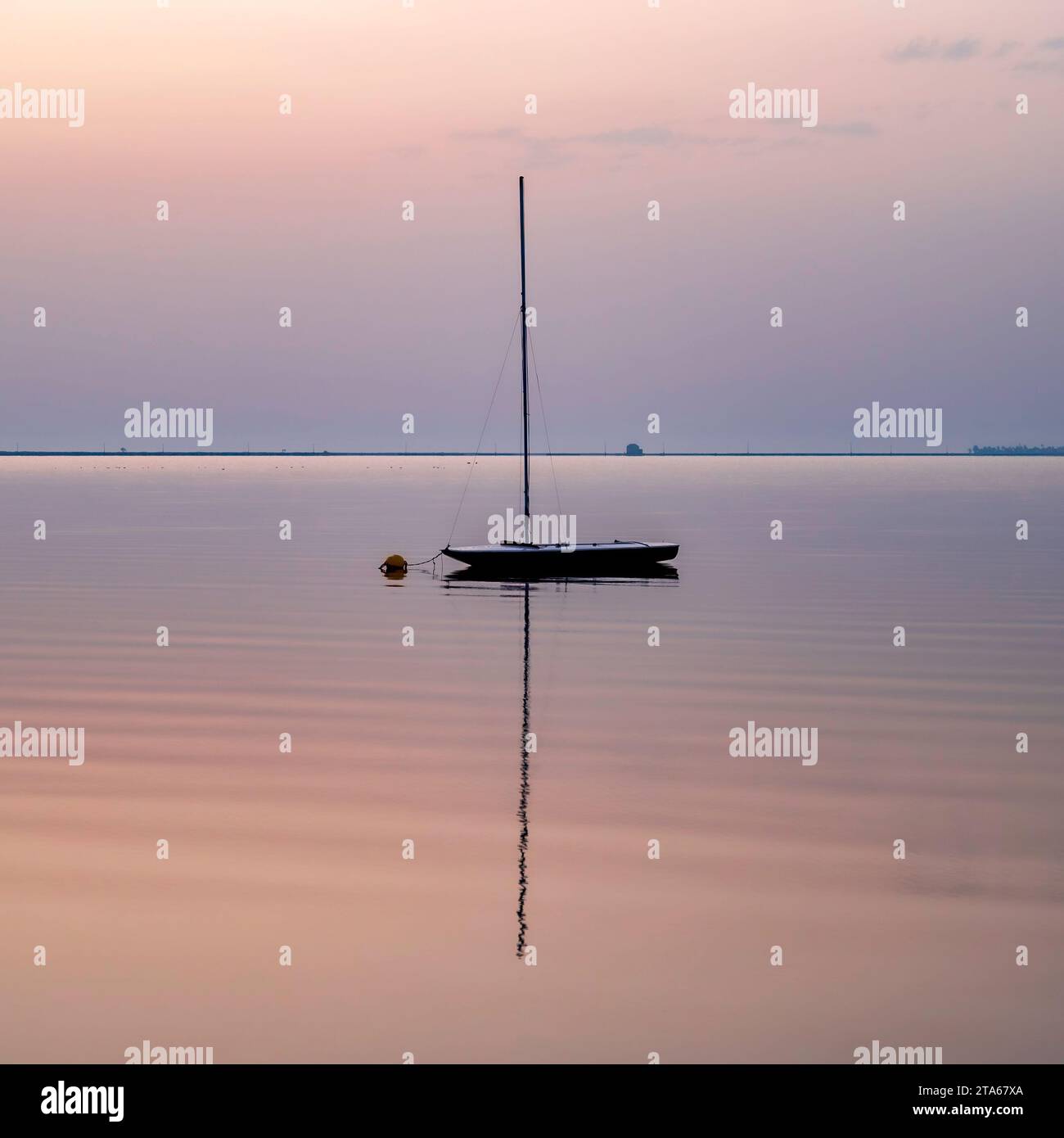 Un'unica barca a vela, riflessa nelle calme acque del Mediterraneo, all'alba Foto Stock