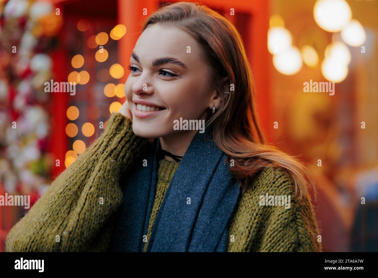 Ritratto di una giovane donna sorridente che si gode in vacanza di ghirlande luminose su una strada decorata della città. Vista ravvicinata. Foto Stock