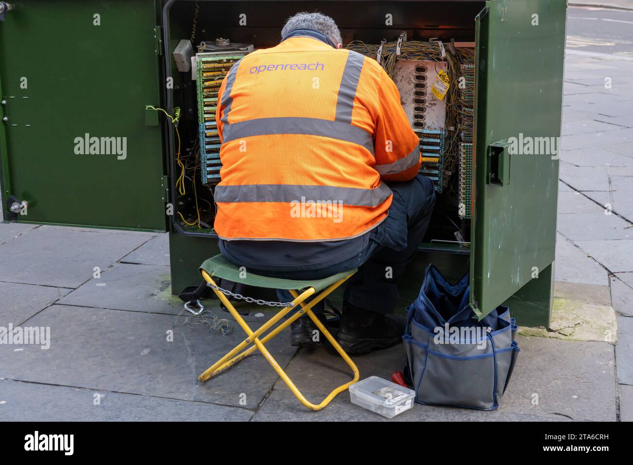Un ingegnere Openreach si siede per riparare un armadio verde in strada. Concetto di FTTC, banda larga, connettività. Foto Stock
