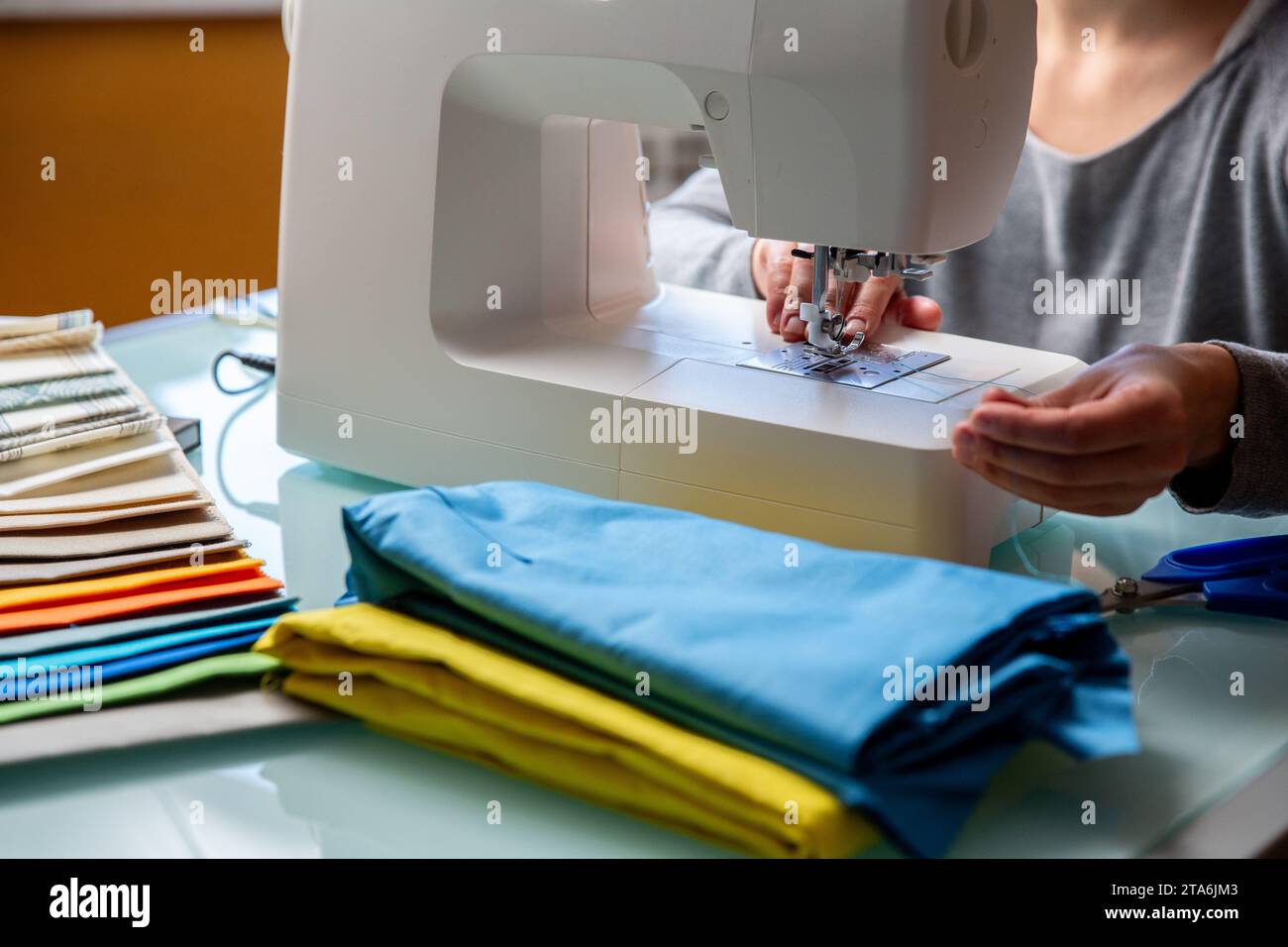 Primo piano delle mani femminili di Tailor che preparano la macchina da cucire. Campioni di tessuto inclusi Foto Stock