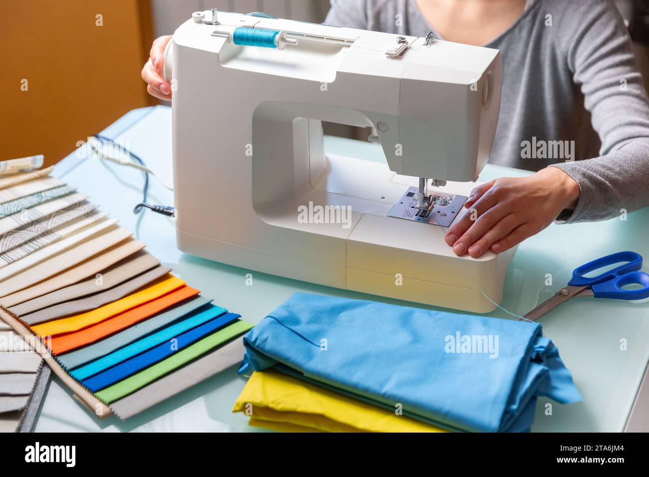 Primo piano delle mani femminili di Tailor che preparano la macchina da cucire. Campioni di tessuto inclusi Foto Stock