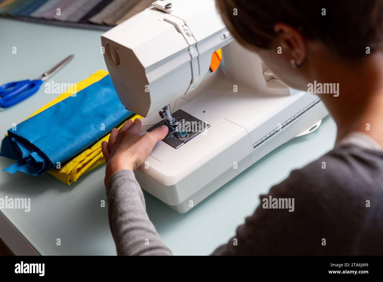 Primo piano delle mani femminili di Tailor che preparano la macchina da cucire. Campioni di tessuto inclusi Foto Stock