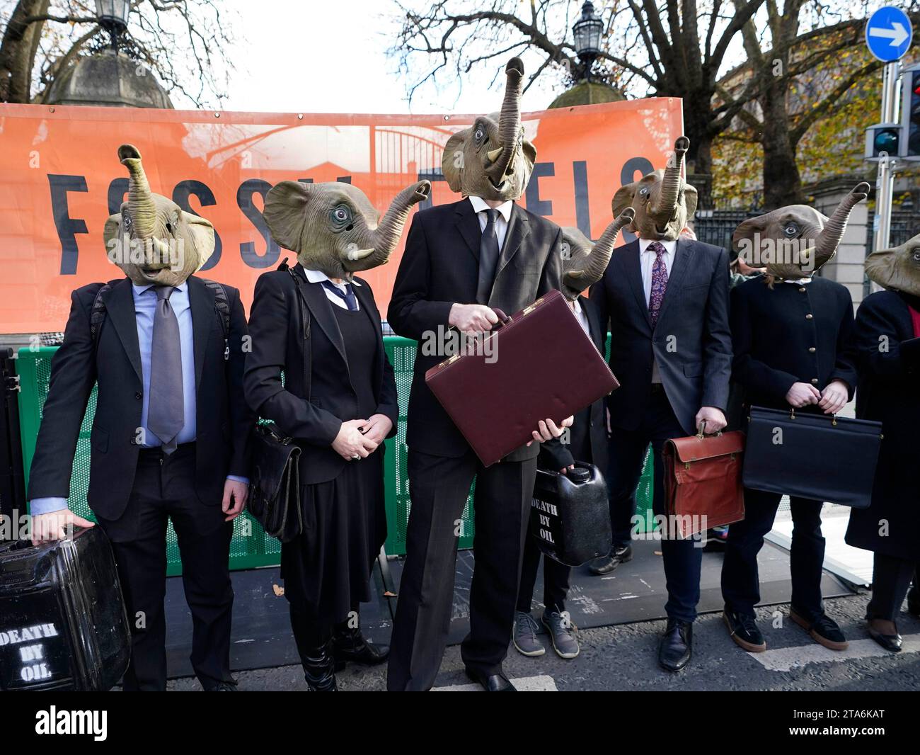 Fermare i membri del caos climatico, vestiti da CEO della Big Oil, con abiti da lavoro neri e con maschere di elefante fuori dalla Leinster House di Dublino per avvertire il governo irlandese che non deve lasciare che i combustibili fossili distruttivi dal clima siano l'elefante nella stanza dei colloqui sul clima della COP28 delle Nazioni Unite. Data foto: Mercoledì 29 novembre 2023. Foto Stock