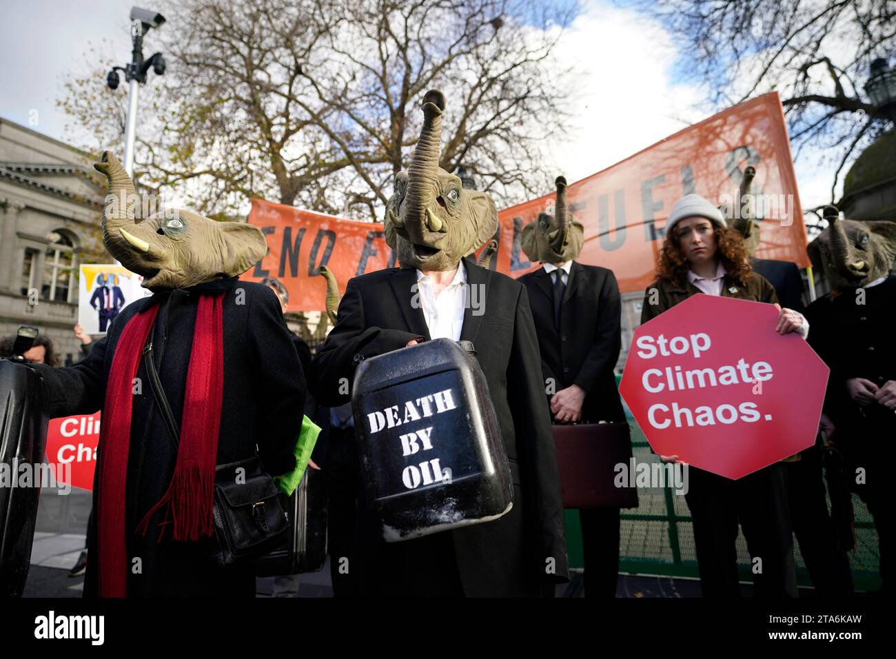 Fermare i membri del caos climatico, vestiti da CEO della Big Oil, con abiti da lavoro neri e con maschere di elefante fuori dalla Leinster House di Dublino per avvertire il governo irlandese che non deve lasciare che i combustibili fossili distruttivi dal clima siano l'elefante nella stanza dei colloqui sul clima della COP28 delle Nazioni Unite. Data foto: Mercoledì 29 novembre 2023. Foto Stock