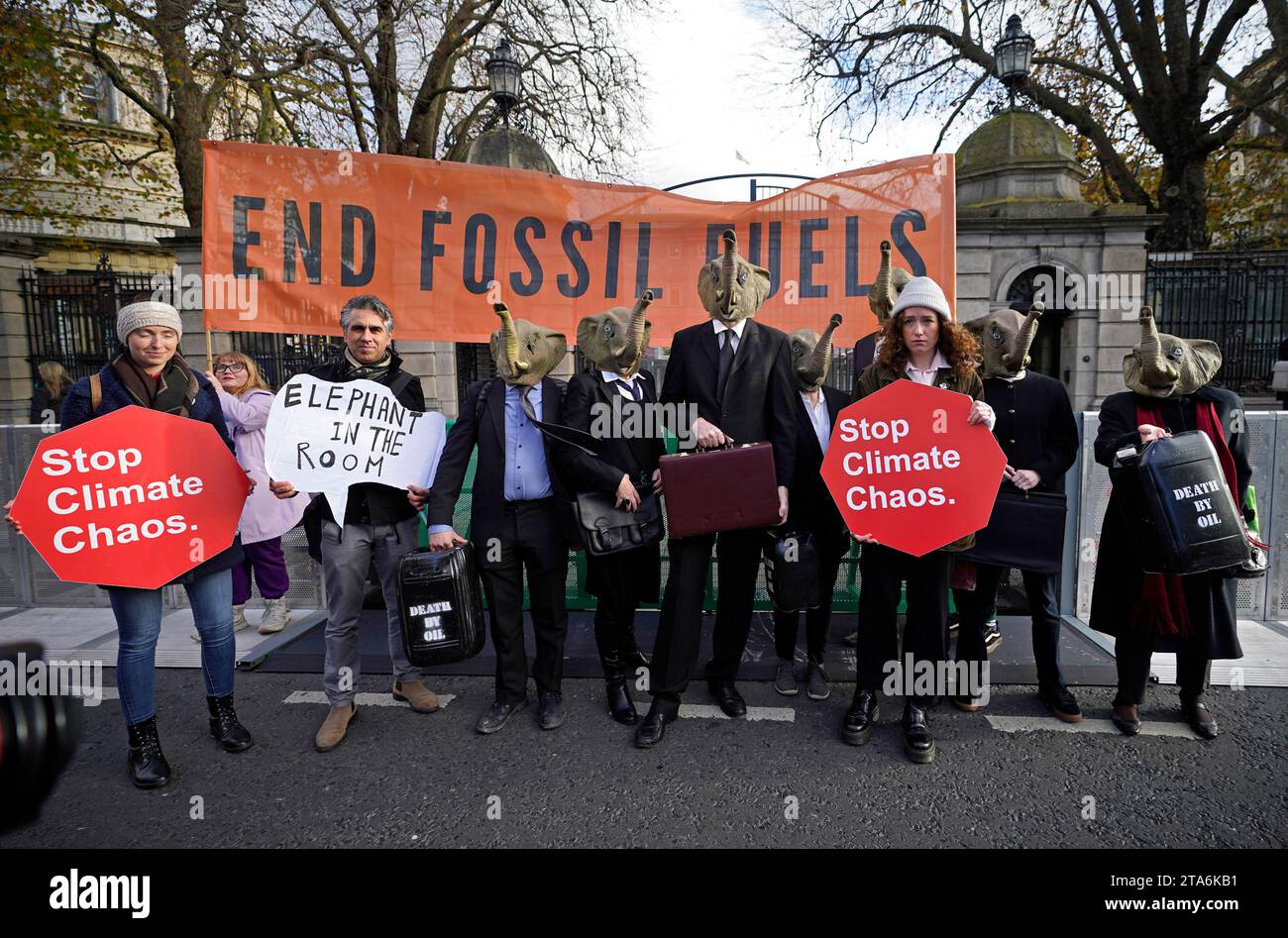 Fermare i membri del caos climatico, vestiti da CEO della Big Oil, con abiti da lavoro neri e con maschere di elefante fuori dalla Leinster House di Dublino per avvertire il governo irlandese che non deve lasciare che i combustibili fossili distruttivi dal clima siano l'elefante nella stanza dei colloqui sul clima della COP28 delle Nazioni Unite. Data foto: Mercoledì 29 novembre 2023. Foto Stock