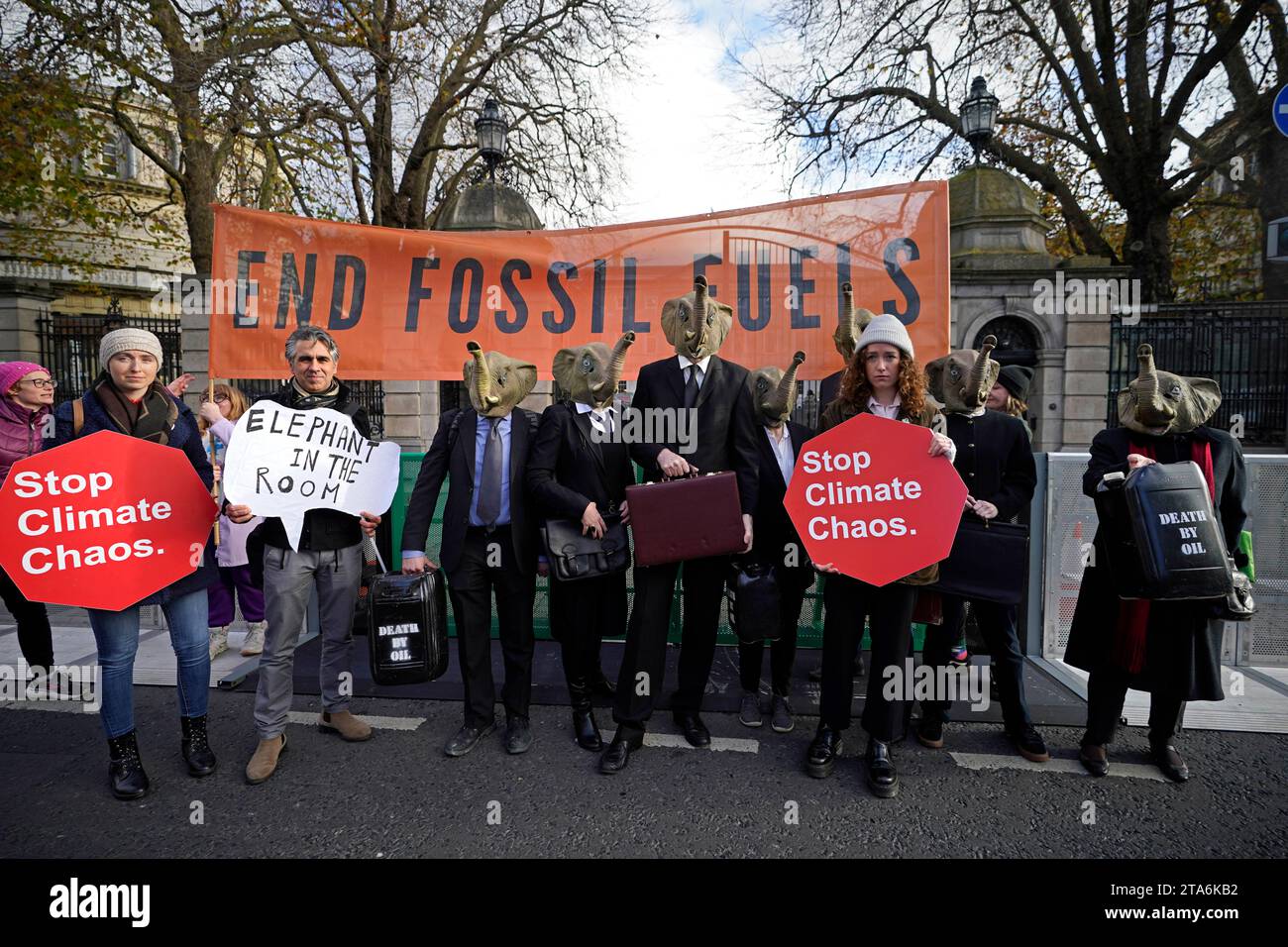 Fermare i membri del caos climatico, vestiti da CEO della Big Oil, con abiti da lavoro neri e con maschere di elefante fuori dalla Leinster House di Dublino per avvertire il governo irlandese che non deve lasciare che i combustibili fossili distruttivi dal clima siano l'elefante nella stanza dei colloqui sul clima della COP28 delle Nazioni Unite. Data foto: Mercoledì 29 novembre 2023. Foto Stock