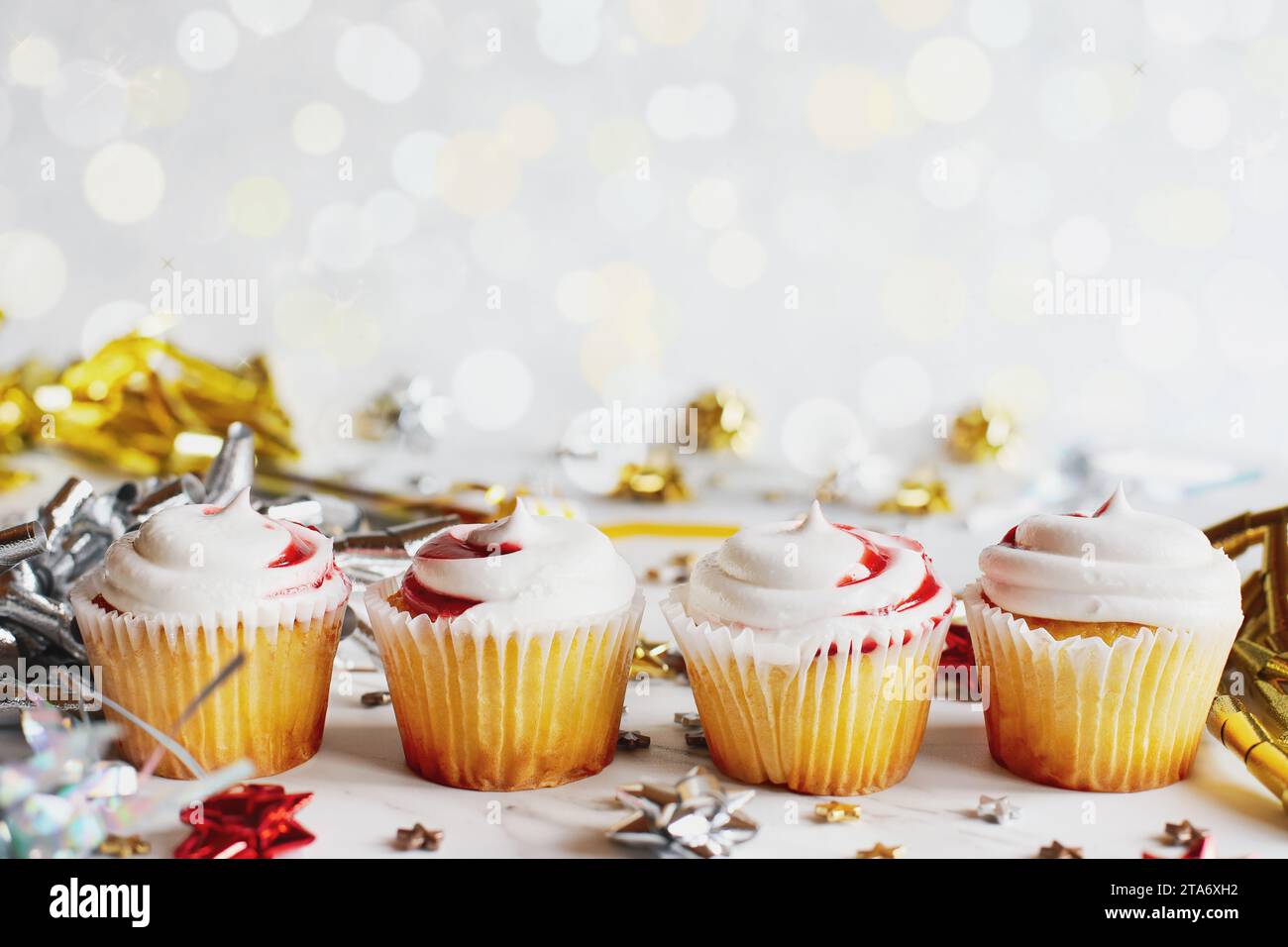 Quattro cupcake alla vaniglia con glassa a vortice di fragole allineati per una festa tra fiocchi di nastro e coriandoli. Messa a fuoco selettiva con sfondo sfocato. Foto Stock