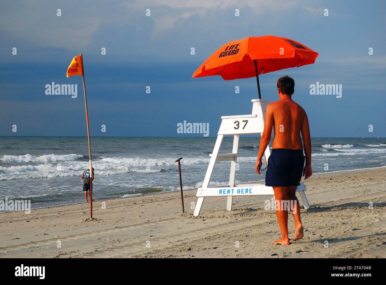 Un giovane uomo prepara la sedia e l'ombrellone del bagnino prima che la folla arrivi sulla riva di Myrtle Beach, South Carolina Foto Stock