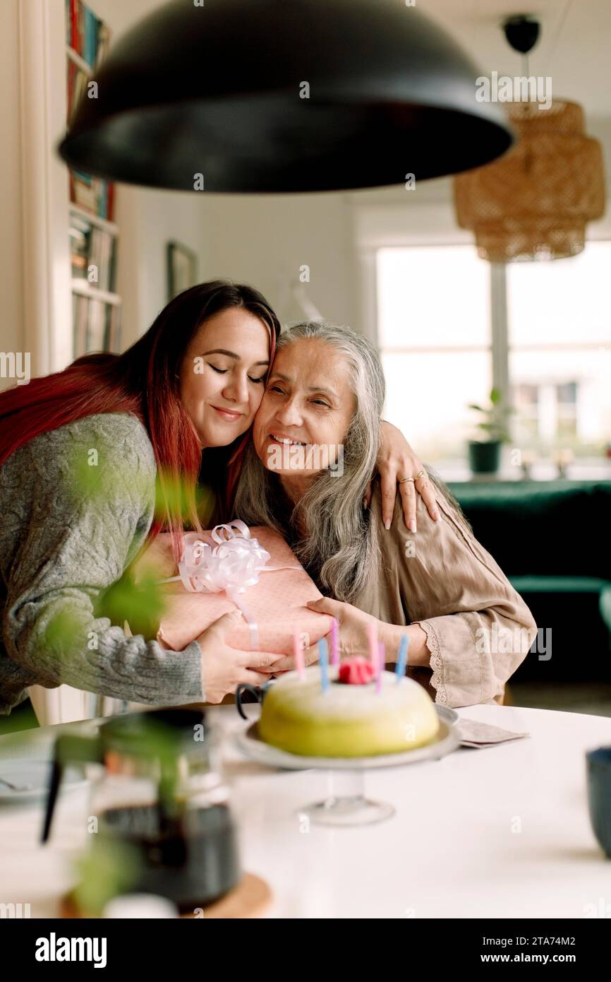 Donna sorridente che abbraccia la madre e fa un regalo di compleanno a casa Foto Stock