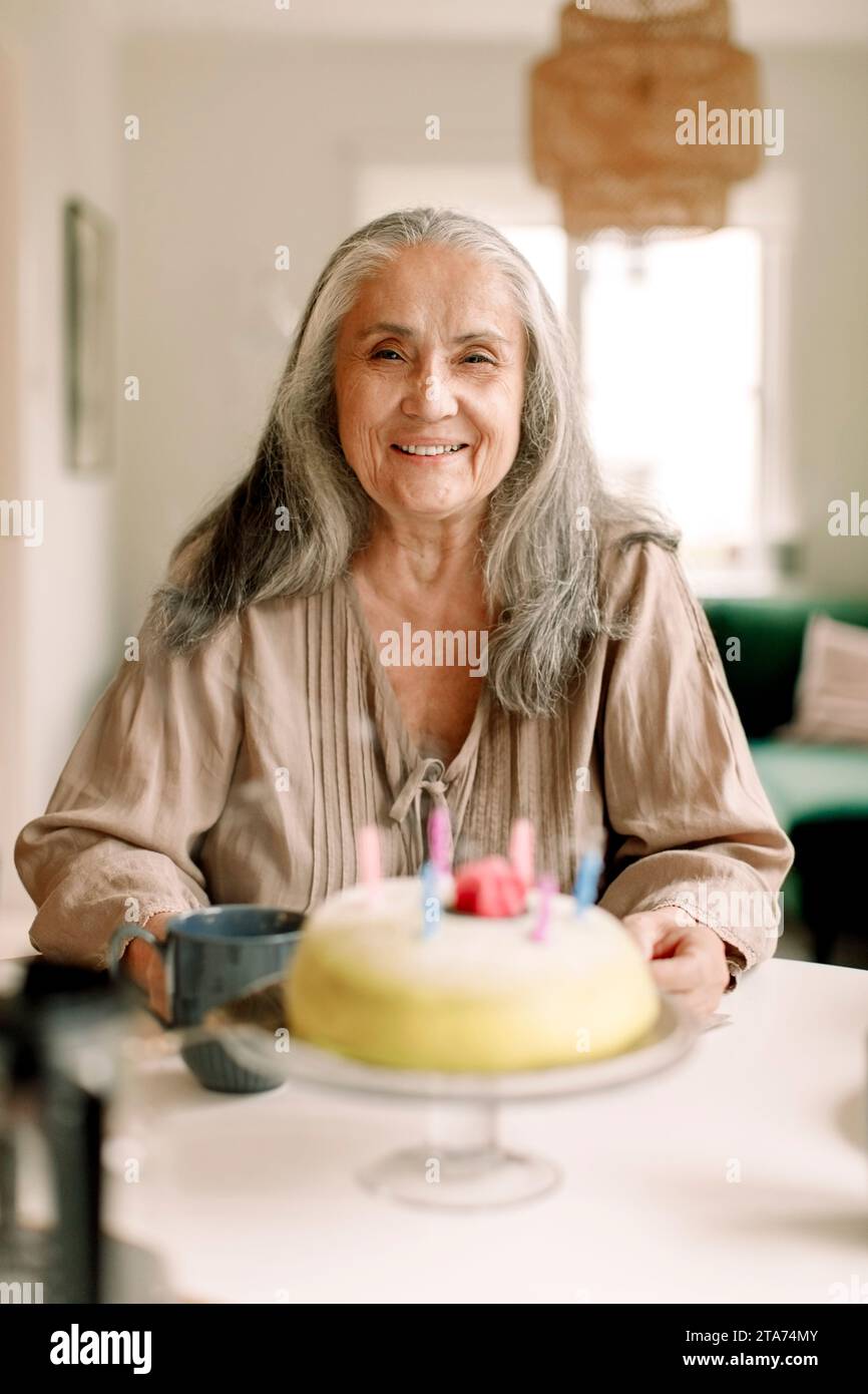 Ritratto di donna anziana sorridente con torta di compleanno sul tavolo a casa Foto Stock