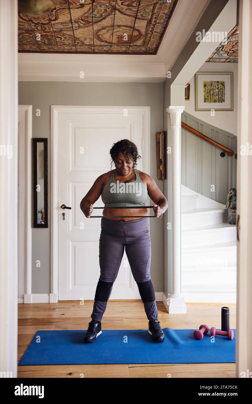 Donna matura che si allena con la fascia di resistenza sul tappetino da ginnastica a casa Foto Stock