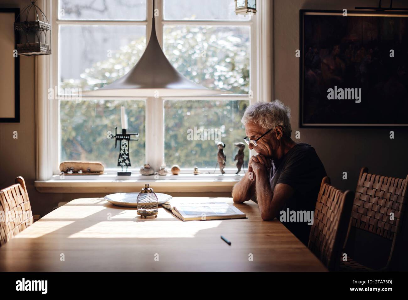 Uomo anziano con occhiali che legge un libro sul tavolo a casa Foto Stock