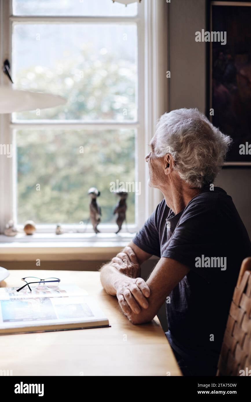 Uomo anziano che guarda dalla finestra mentre è seduto a casa Foto Stock