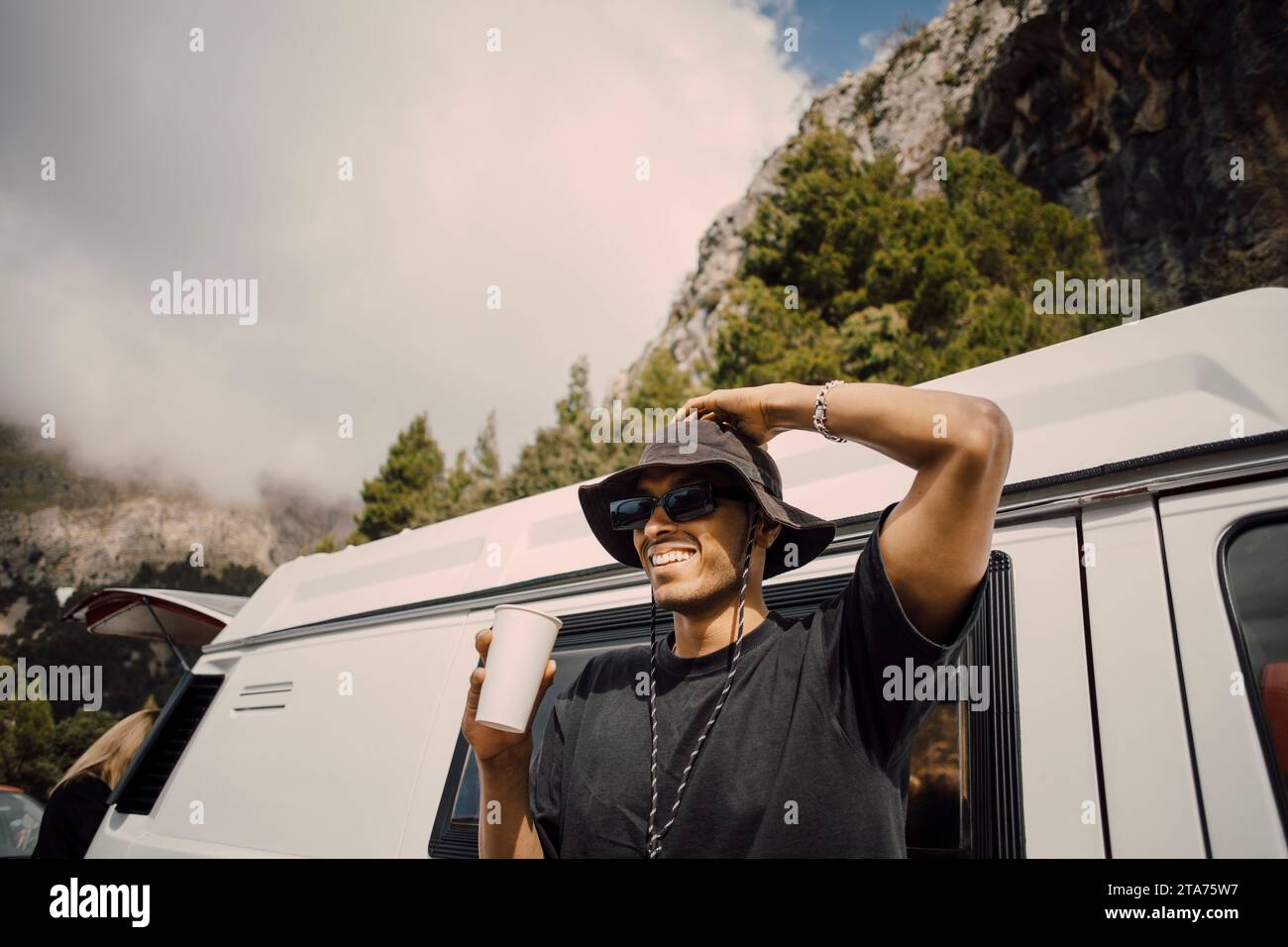 Giovane sorridente con la testa in mano che regge un bicchiere vicino al furgone Foto Stock