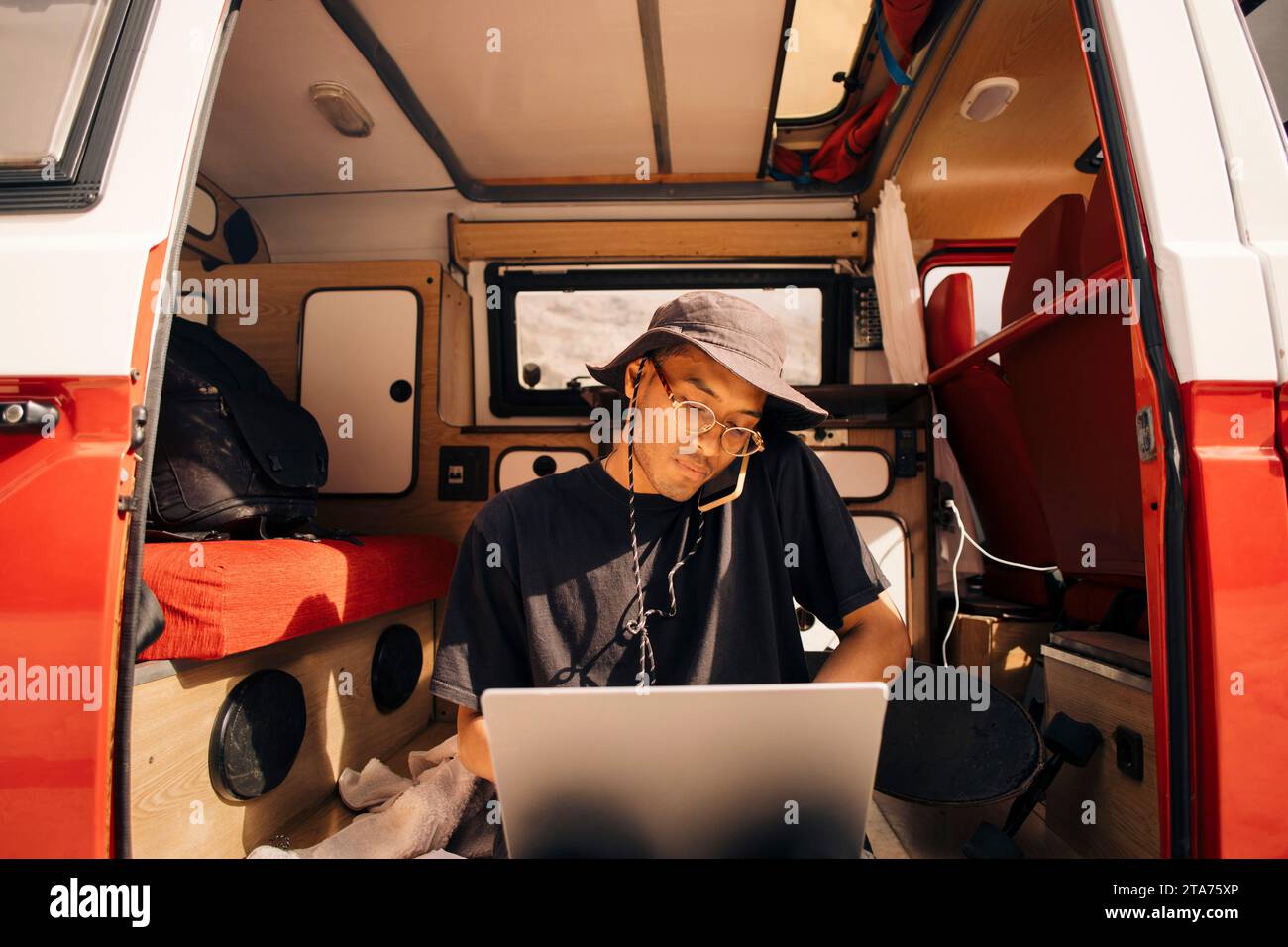 Giovane uomo che lavora in multitasking mentre è seduto nel furgone durante le vacanze Foto Stock