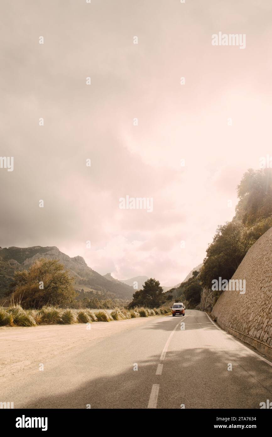 Pulmino che si muove su strada contro le montagne durante il giorno di sole Foto Stock