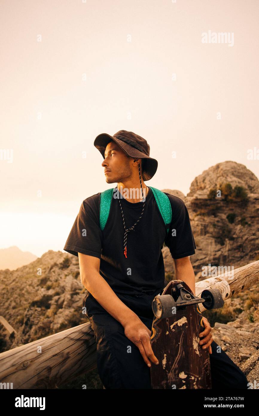 Giovane seduto su una ringhiera con lo skateboard Foto Stock
