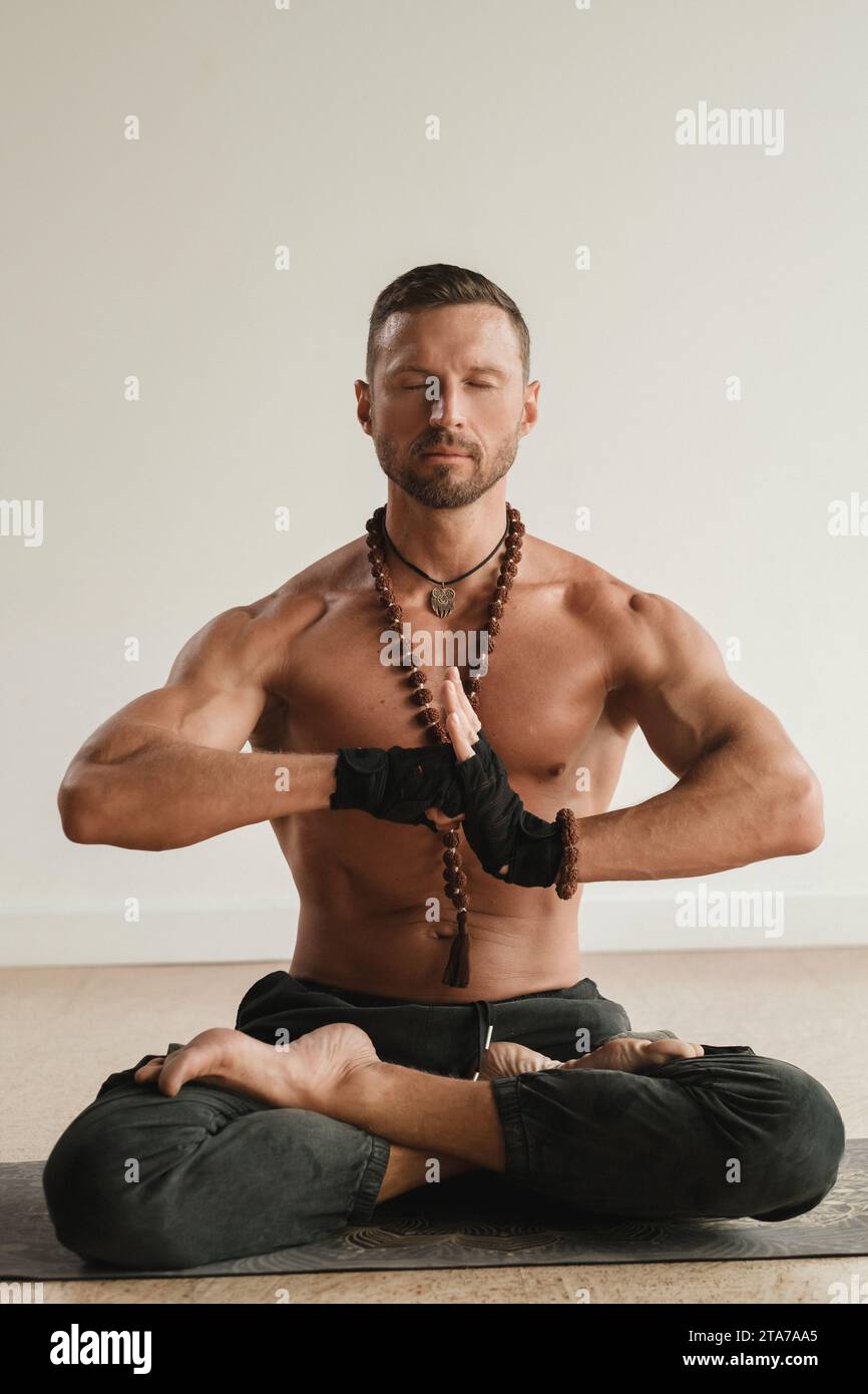 un uomo con il torso nudo è seduto in posizione di loto prima di fare yoga in casa. Fitness Trainer. Foto Stock
