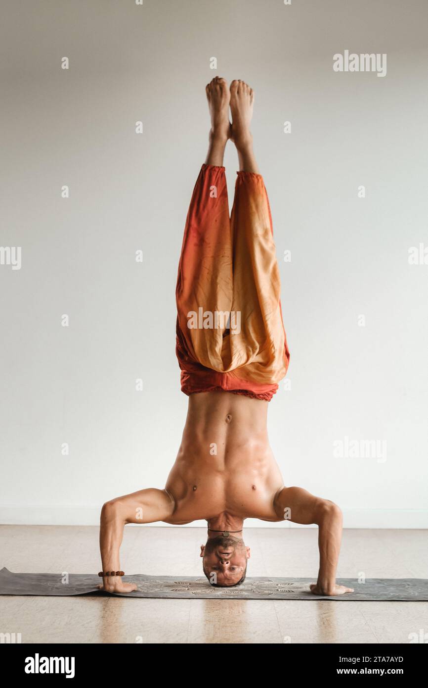 un uomo con un torso nudo fa yoga in piedi sulla testa al chiuso. Fitness Trainer. Foto Stock