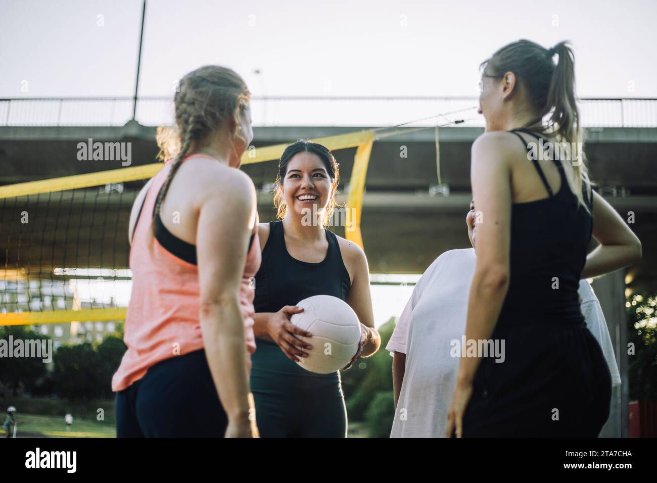 Vista dall'angolo basso di una donna sorridente che tiene una pallavolo con amici femminili Foto Stock